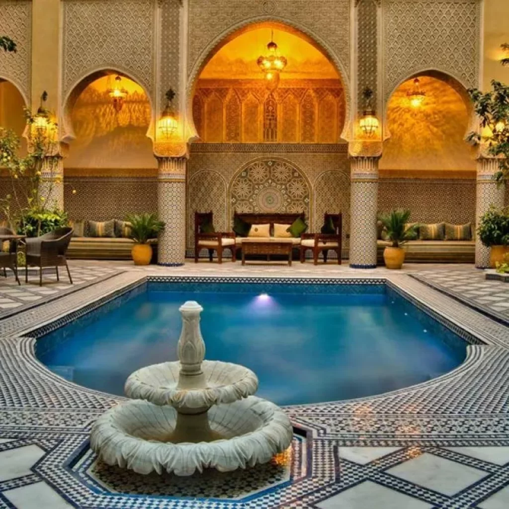 A large indoor swimming pool with a fountain inside a traditionnal Riads while your Morocco Luxury Tours