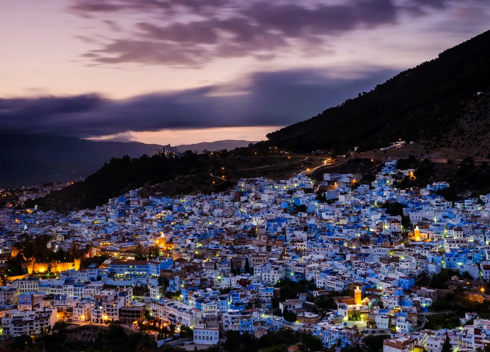 A whole blue city of Chefchaouen which is lit up at night with a mountain in the background while your 12-day Morocco luxury tour from Casablanca