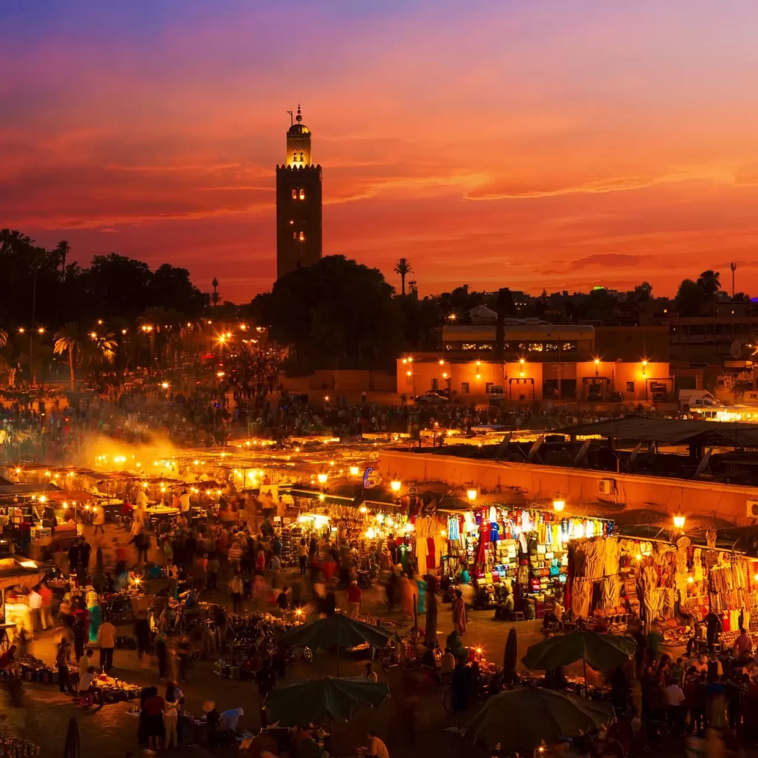 1. A panoramic view of Marrakech at dusk, showcasing vibrant colors in the sky and illuminated buildings against the horizon while your 16-day Morocco luxury tour from Casablanca