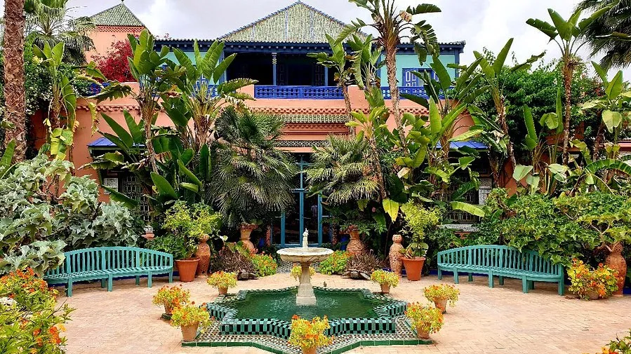 A serene garden in a Marrakech Jardins MAjorelle, featuring lush greenery, vibrant flowers, and traditional Moroccan architecture.