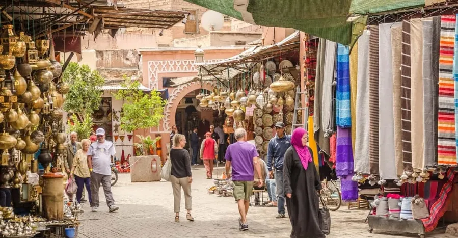 Vibrant market scene with people strolling among stalls displaying an array of colorful fabrics in Medina of Marrakech