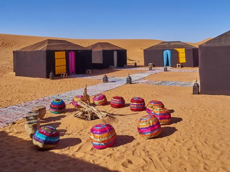 A vibrant desert camp in Merzouga featuring colorful tents surrounding a cozy fire pit under a clear night sky.