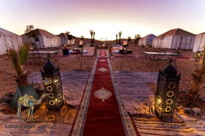  A desert camp in Merzouga featuring tents arranged on a vibrant red carpet under a clear blue sky.