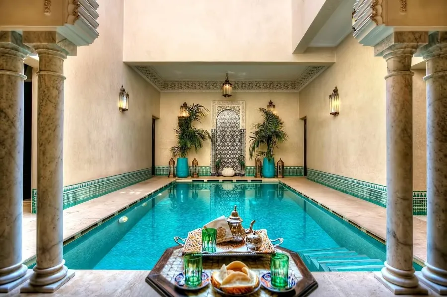 A pool surrounded by a table and chairs, situated in the center of a modern luxurious Riad in Marrakech