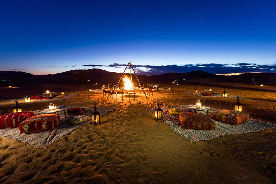 A glowing fire pit surrounded by desert sand under a starry night sky, creating a warm and inviting atmosphere.